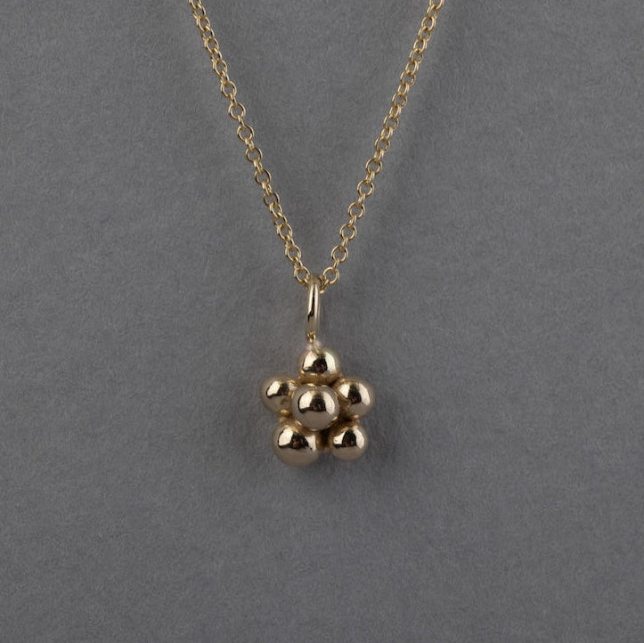 A gold chain necklace with a small blackberry pendant, displayed against a solid gray background.