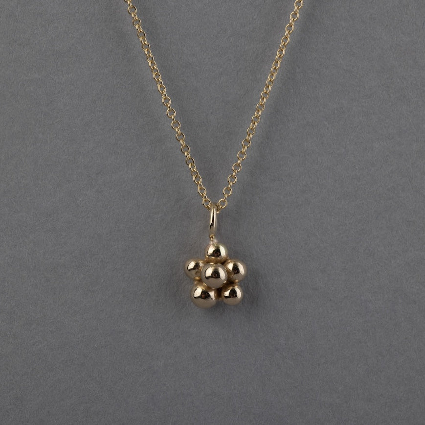 A gold chain necklace with a small blackberry pendant, displayed against a solid gray background.
