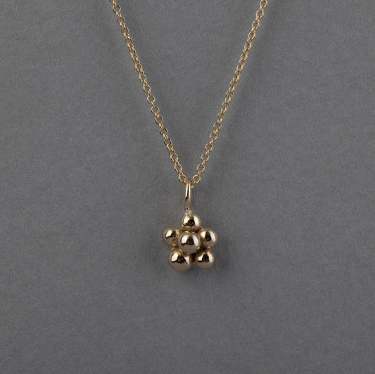 A gold chain necklace with a small blackberry pendant, displayed against a solid gray background.